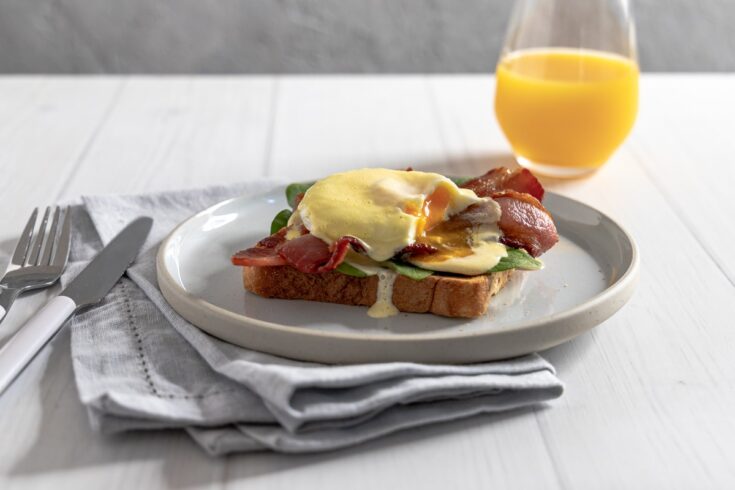 Easy at home eggs benedict with bacon and spinach served with orange juice