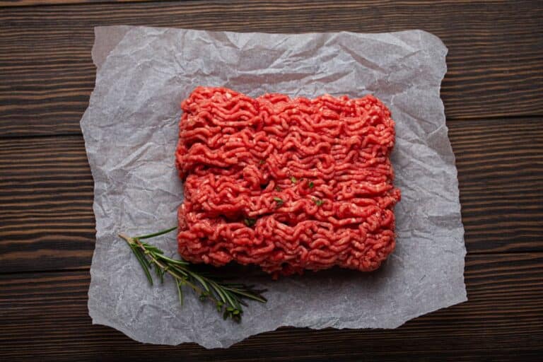raw ground beef on paper on timber background with rosemary and thyme