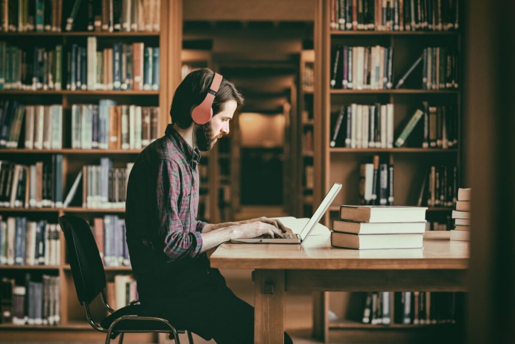 man wearing headphones and working on laptop in the library. Representing free things from the library