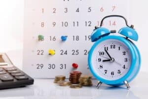 calendar with pins in it and clock and calculator and coins depicting managing the bills