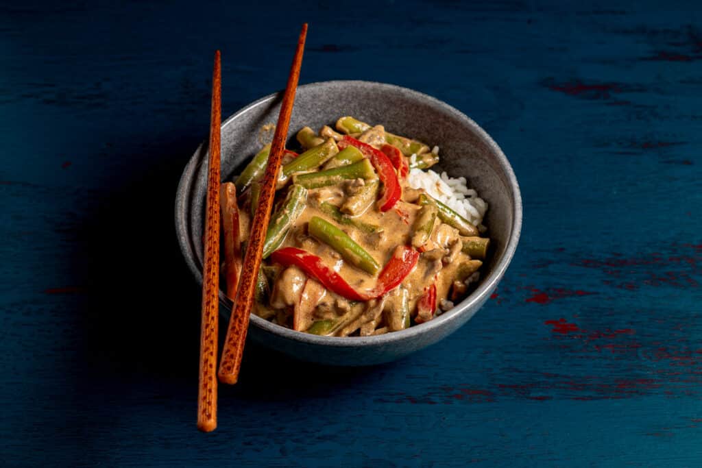 thai beef curry in a bowl with rice and chopsticks, blue background