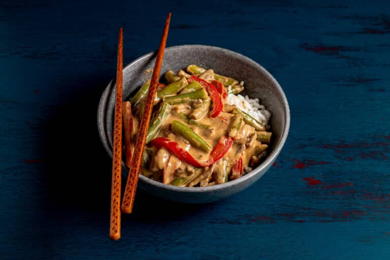 thai beef curry in a bowl with rice and chopsticks, blue background