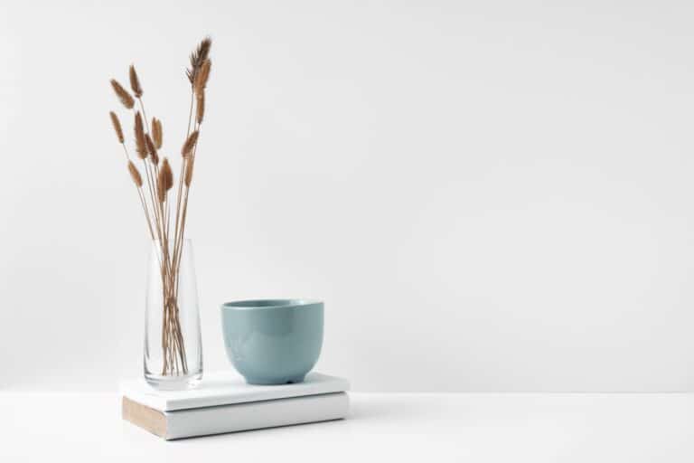 vase of pussy willow with mug on pile of books, minimalist white tableau