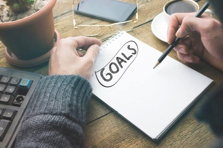 man writing goals down on pad of paper