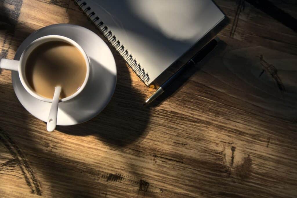 coffee on a timber table beside a notebook and pen
