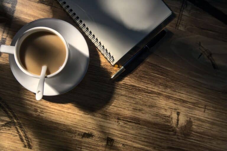 coffee on a timber table beside a notebook and pen