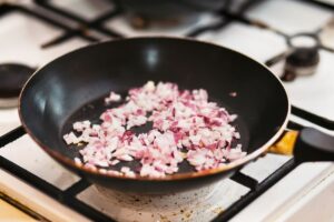 pan sautéing onion on stove, representing cooking methods to learn