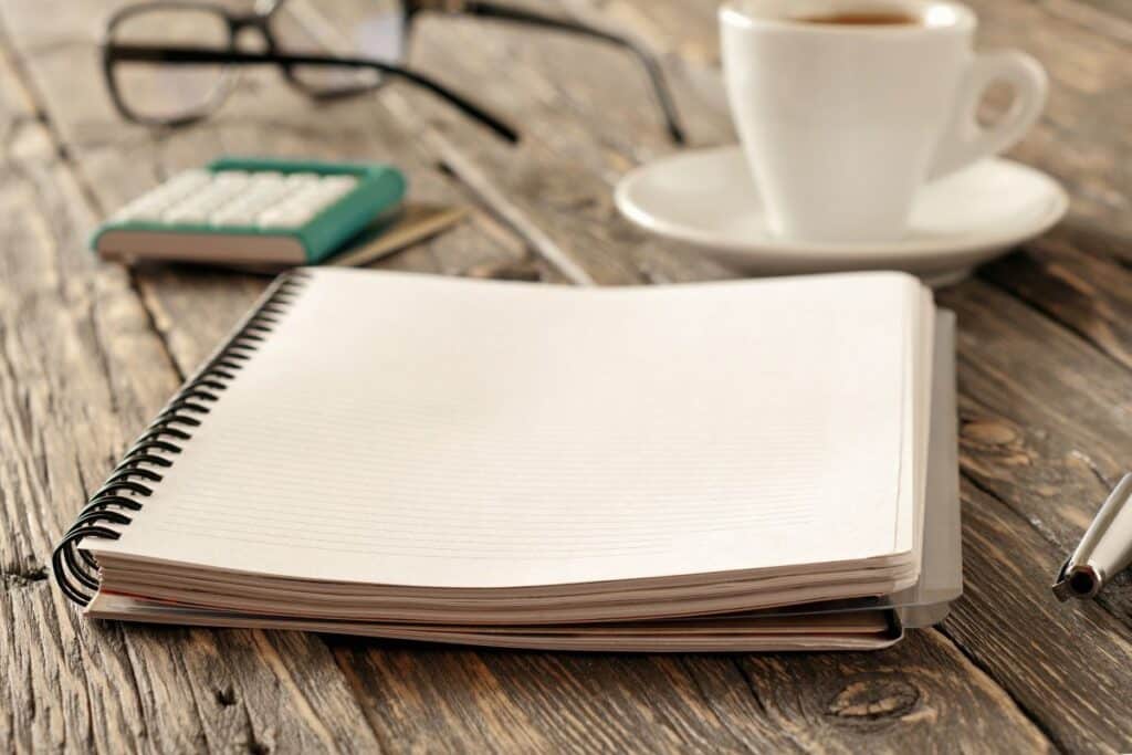 notebook, coffee, pen, calculator on timber desk representing survival budget planning