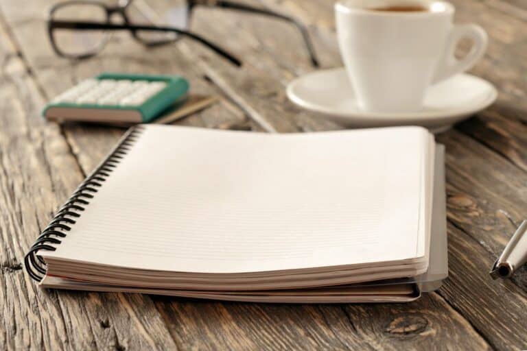 notebook, coffee, pen, calculator on timber desk representing survival budget planning