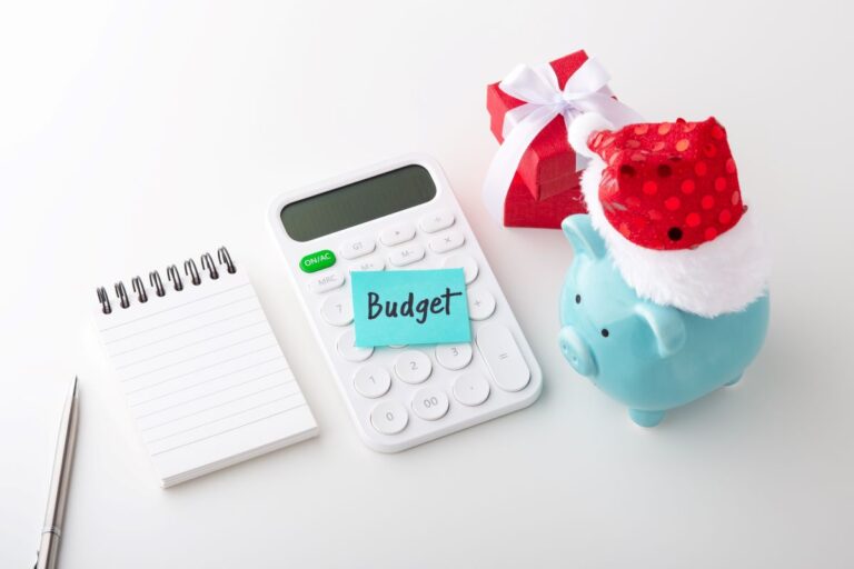 calculator next to piggy bank wearing santa hat, gift, pen and writing pad