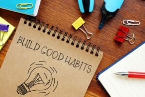 note pad with light bulb on it and build good habits written on table with miscellaneous stationary