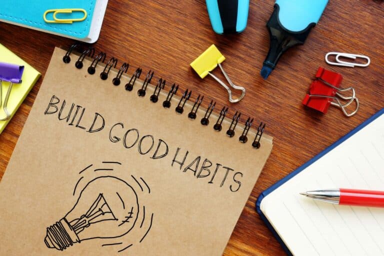 note pad with light bulb on it and build good habits written on table with miscellaneous stationary