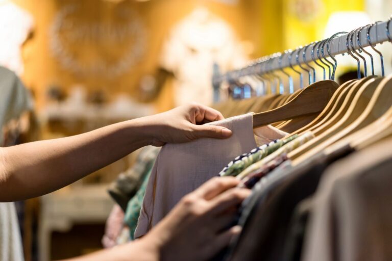 woman's hand looking through clothing rack representing ways to save money on clothes